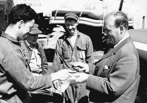 Gluckmann, surrounded by clearly bemused US Air Force personnel, paying for fuel with cash.  A full 90 gallons would have cost him $23.40. Photo: Fritz Adam 