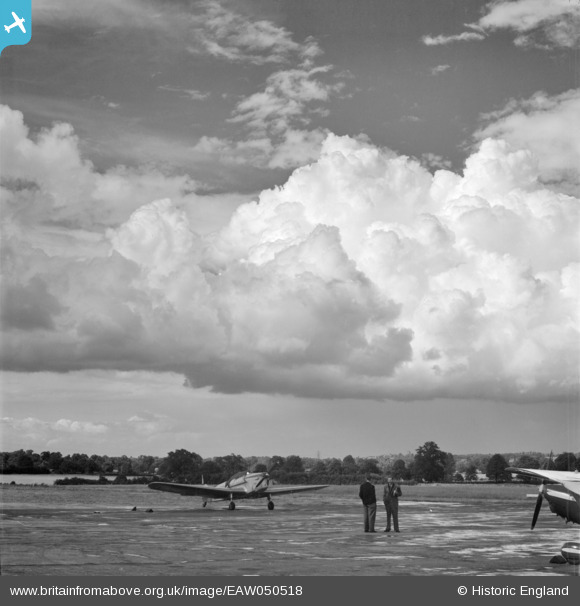 Luscombe 8 (N1838B) at Elstree Aerodrome, Aldenham near London in June 1953 (or possibly July 9, 1953). This could be showing Gluckmann speaking with someone else at the airport. His aircraft is on the right in the foreground. The airplane in the background appears to be a Dehavilland Chipmunk.  It is unclear if this photograph was taken before or after his flight to Berlin-Tempelhof. Photographer unknown. britainfromabove.org.uk/en/image/EAW050518 