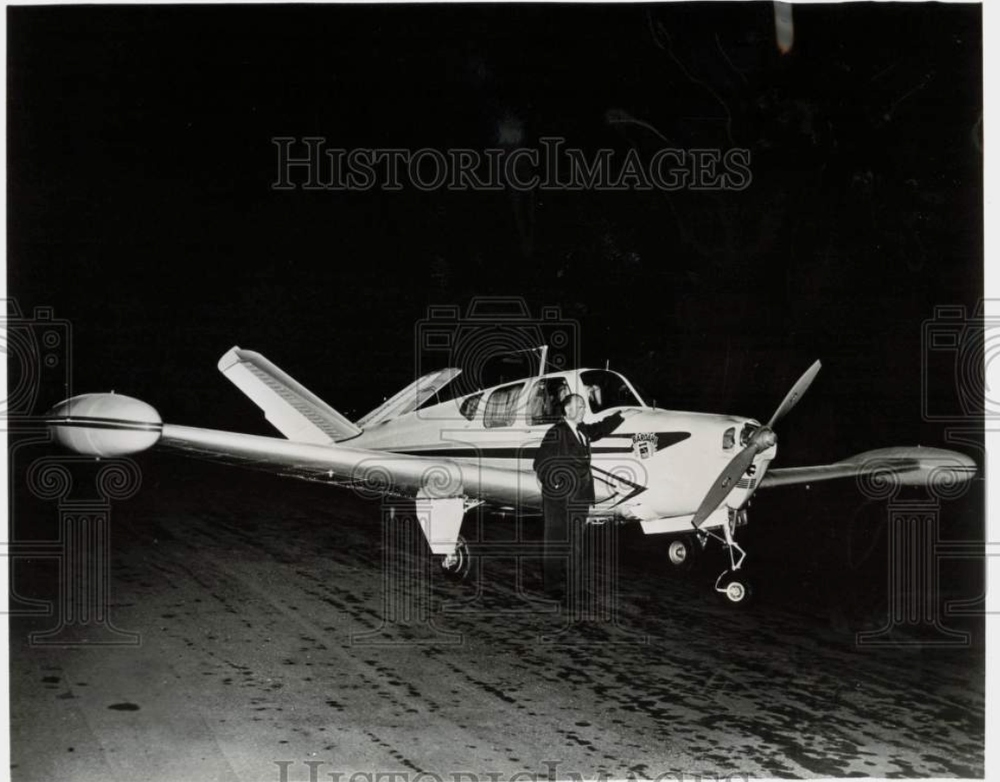 This appears to be a press release promo photo for Bardahl Oil likely in 1960. Caption reads: PILOT PETER GLUCKMANN EXAMINES HIS J-35 BONANZA PLANE. 1960 Gluckmann, Peter (Pilot). Peter Gluckmann is shown beside his extensively modified J-35 Bonanza in which he is attempting to break the existing small plane distance record of 7668.48 miles. Gluckmann, the 34-year-old 'Flying Watchmaker' from San Francisco, hopes to solo non-stop Hong Kong to the western United States” a distance of more than 8000 miles. Lubricated with Bardahl additive oils, the plane will leave the Far East sometime between April 10 and May 1 when weather conditions are most favorable. Where he lands in the United States of America will again depend on the weather as he will select a landing site blessed with favorable tail winds. 